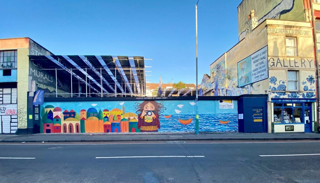 The mural depicting a woman with a camera in front of a Palestinian town by the sea