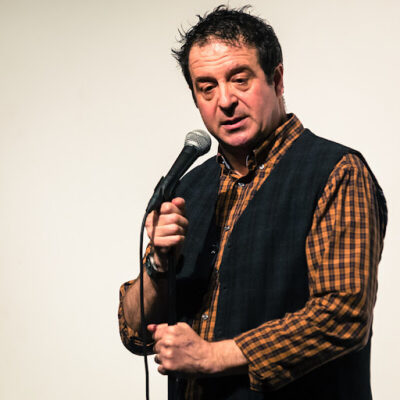 Publicity shot of Mark Thomas holding a microphone